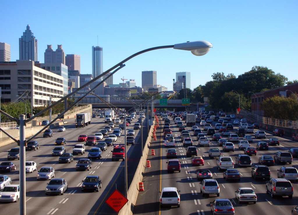A bustling city street filled with pedestrians, cars, and tall buildings under a clear blue sky.